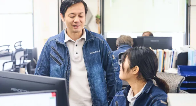 オフィスで先輩社員と若手社員が笑顔で話す様子